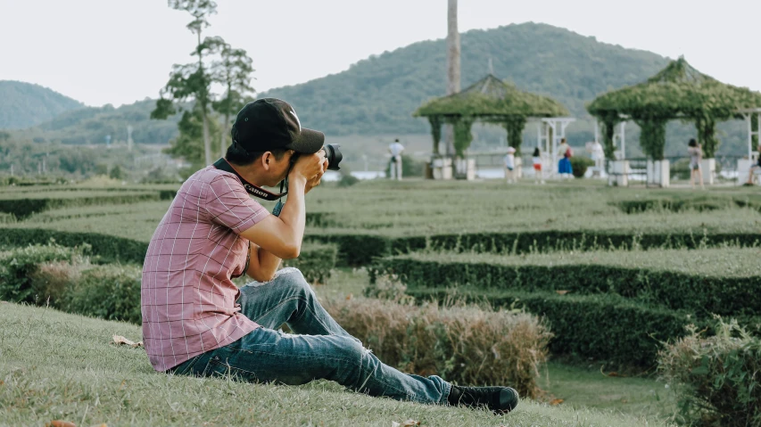 a man sitting on the ground taking a picture, pexels contest winner, parks and gardens, in a scenic background, profile photography, ilustration