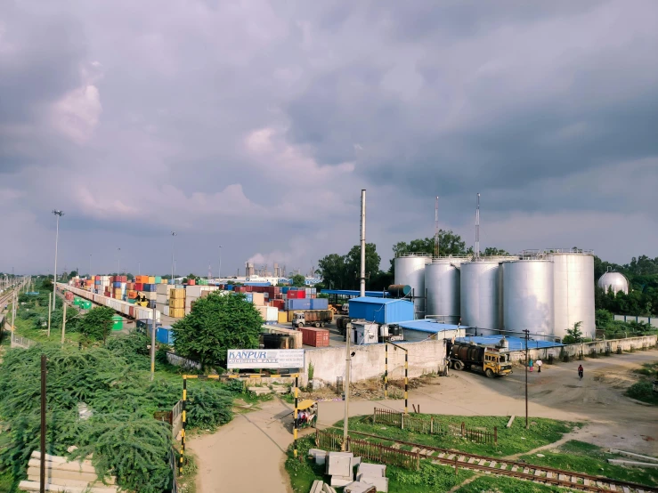 a train traveling down train tracks next to a lush green field, a portrait, unsplash, chemical plant, indore, shipping containers, panorama view of the sky