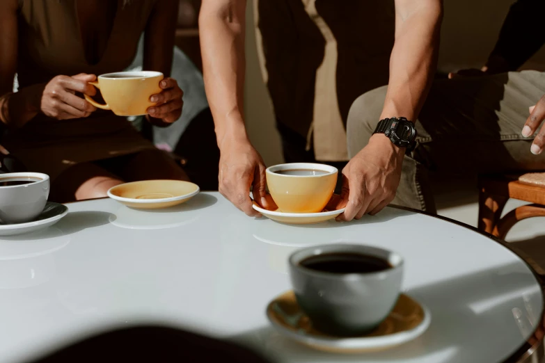 a group of people sitting around a table with cups of coffee, warm coloured, four hands, profile image, zoomed in
