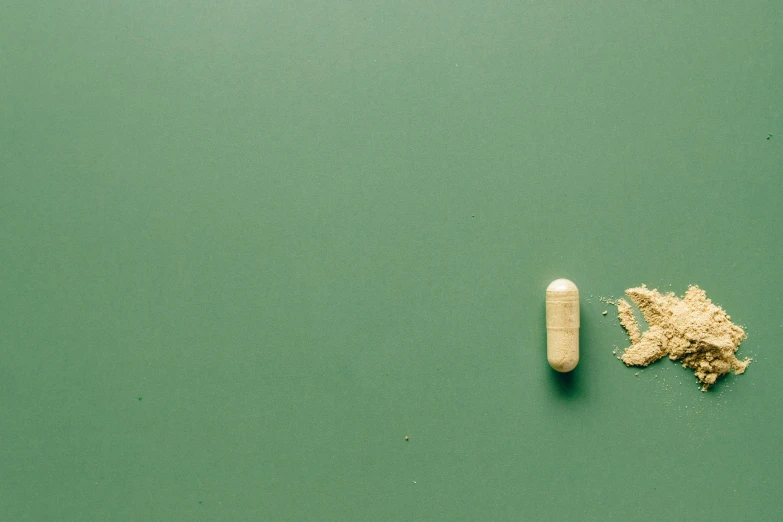 a white pill sitting on top of a green surface, by Elsa Bleda, trending on pexels, postminimalism, gold, maggots, a wooden, panoramic shot