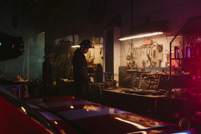 a man standing next to a car in a garage, cyberpunk art, inspired by Elsa Bleda, pexels contest winner, working in the forge, early night, old pawn shop, mechanical features and neon