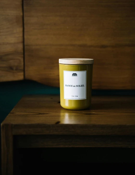 a candle sitting on top of a wooden table, yellow and olive color scheme, product label, skye meaker, shot on hasselblad