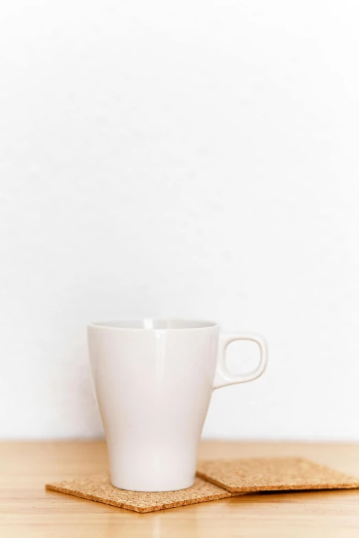 a white cup sitting on top of a wooden table, by Andries Stock, unsplash, minimalism, cream white background, made of glazed, soft light - n 9, mug shot