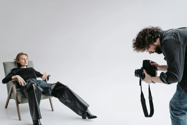 a man taking a picture of a woman sitting in a chair, finn wolfhard, professional studio, wearing leather, dslr +