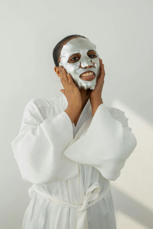 a woman with a sheet mask on her face, wearing silver silk robe, happy face, white pearlescent, adut akech