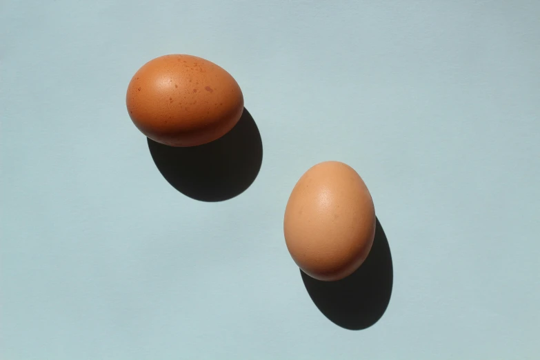 two eggs sitting next to each other on a blue surface, by Jessie Algie, trending on pexels, light tan, shot on hasselblad, profile pic, detailed product image