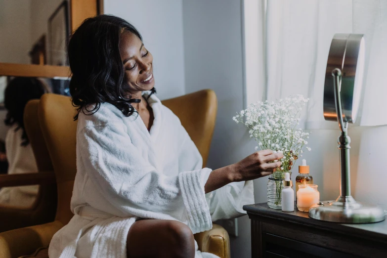 a woman in a bathrobe sitting in a chair, pexels contest winner, african american woman, apothecary, turning her head and smiling, sitting on the edge of a bed