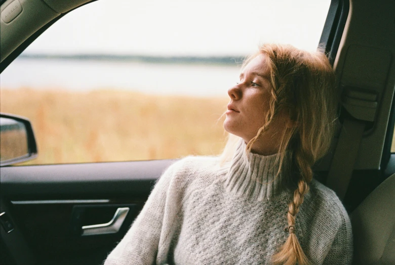 a woman sitting in the passenger seat of a car, trending on unsplash, wearing a sweater, contemplation, sydney sweeney, mild breeze wind