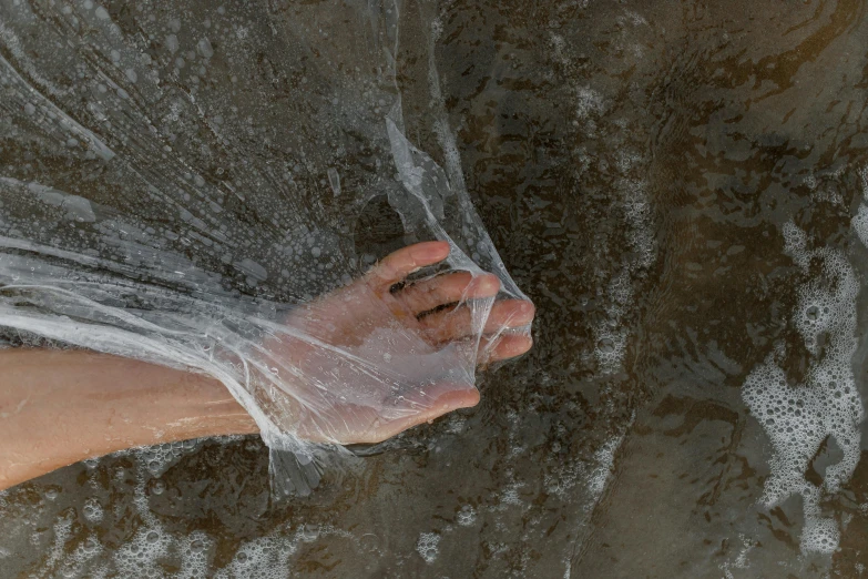 a person holding a plastic bag over a body of water, fountain of water, veiny hands, netting, high quality product image”