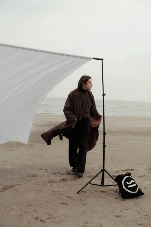 a man standing on top of a sandy beach, inspired by Annie Leibovitz, wearing a brown cape, in a photo studio, wearing a long coat, a24!film cinematography