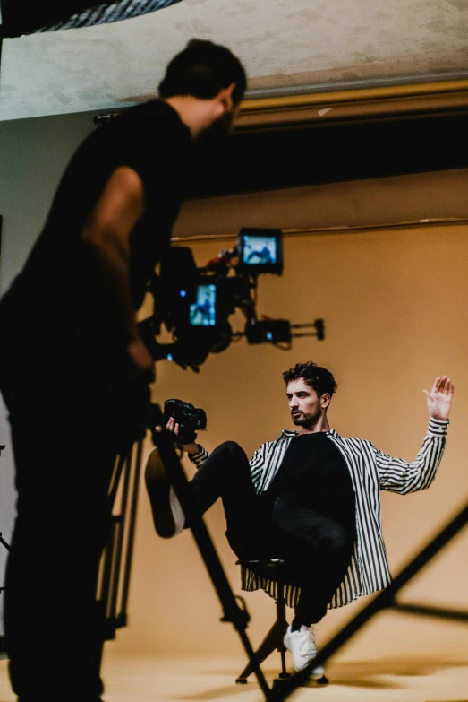 a man sitting in a chair in front of a camera, influencer, facing to audience, at a fashion shoot, ( ( theatrical ) )