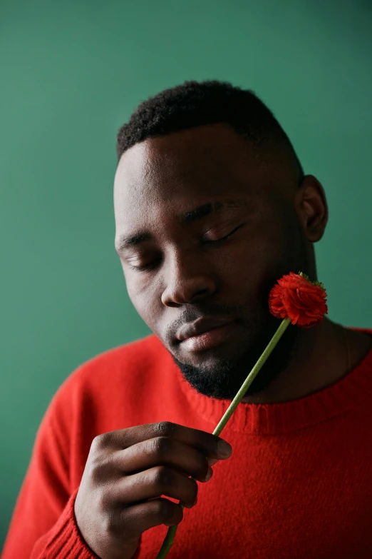 a man holding a flower in front of his face, an album cover, by artist, pexels contest winner, romanticism, ( ( dark skin ) ), wearing a red turtleneck sweater, contemplative, brightly colored