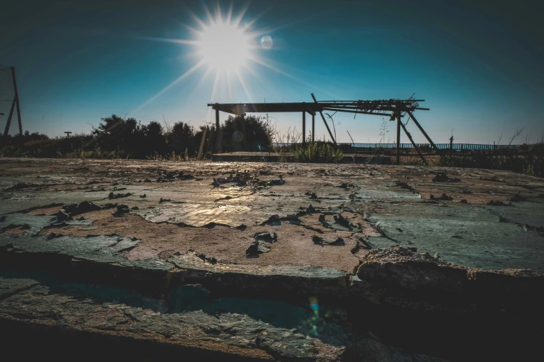 a wooden structure sitting on top of a dirt field, a picture, unsplash, realism, toxic rays of the sun, ruined gas station and cars, shoreline, suns