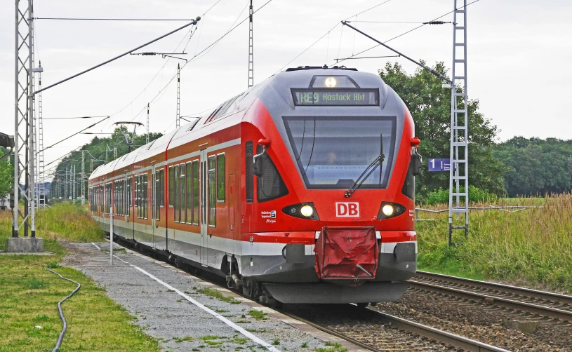 a red train traveling down train tracks next to a lush green field, by Karl Völker, pixabay, train station in summer, public bus, red brown and grey color scheme, diesel engine