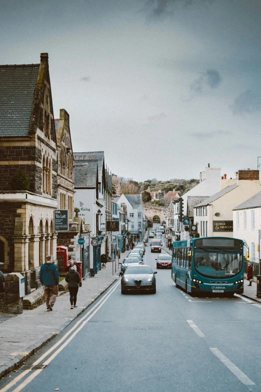 a blue bus driving down a street next to tall buildings, by Rachel Reckitt, pexels contest winner, medieval coastal village, pembrokeshire, people walking around, panoramic shot