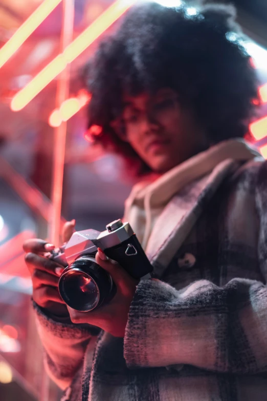 a close up of a person holding a camera, pexels contest winner, afrofuturism, red and cinematic lighting, posing for a picture, blurred, photo of young woman