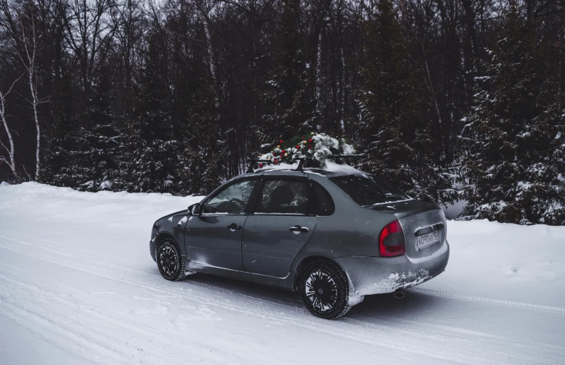 a small car driving down a snow covered road, steel gray body, 🌲🌌