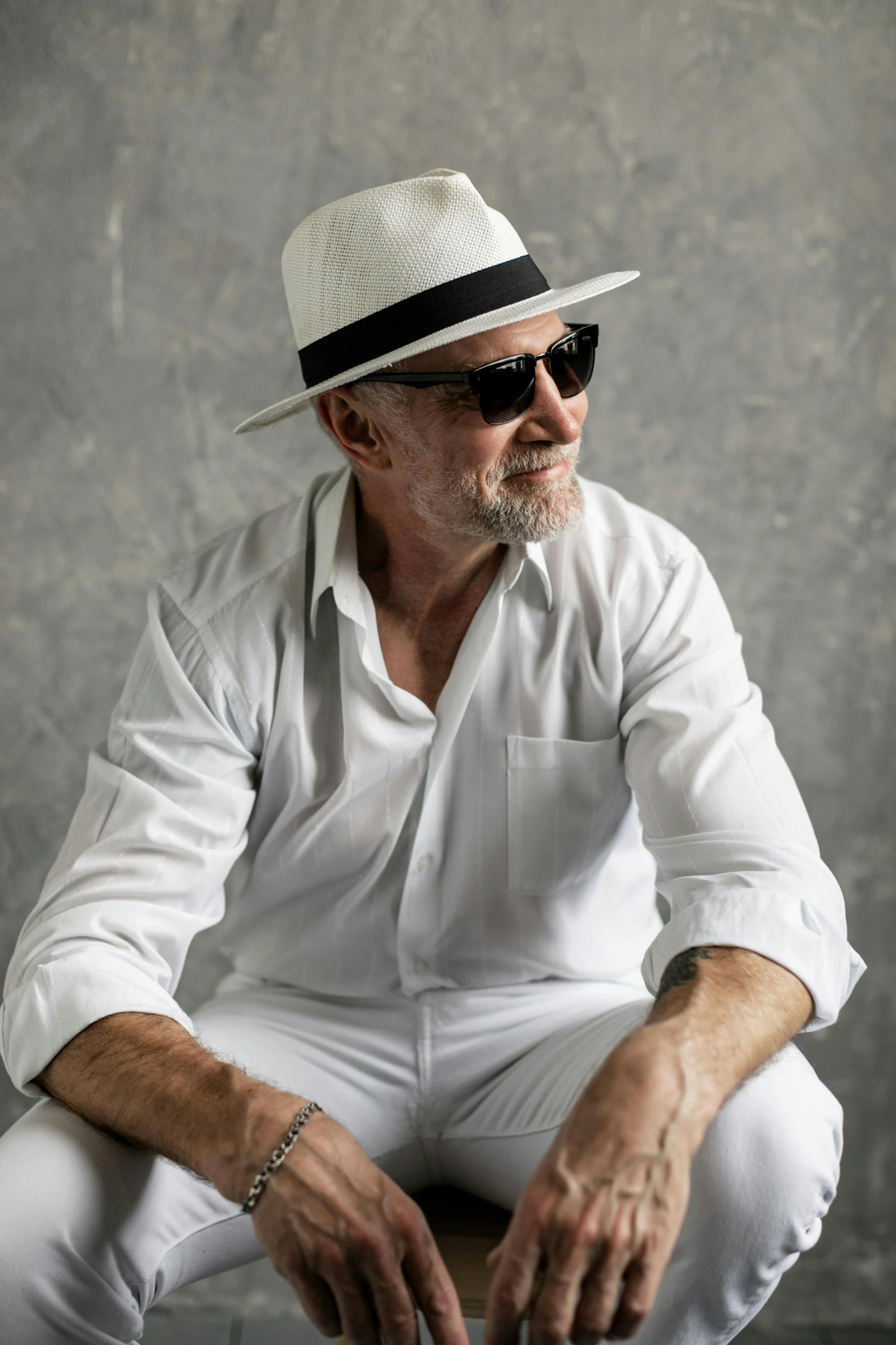 a man in a white shirt and hat sitting on a stool, wearing sunglasses, mike ehrmantraut, stylish pose, profile image
