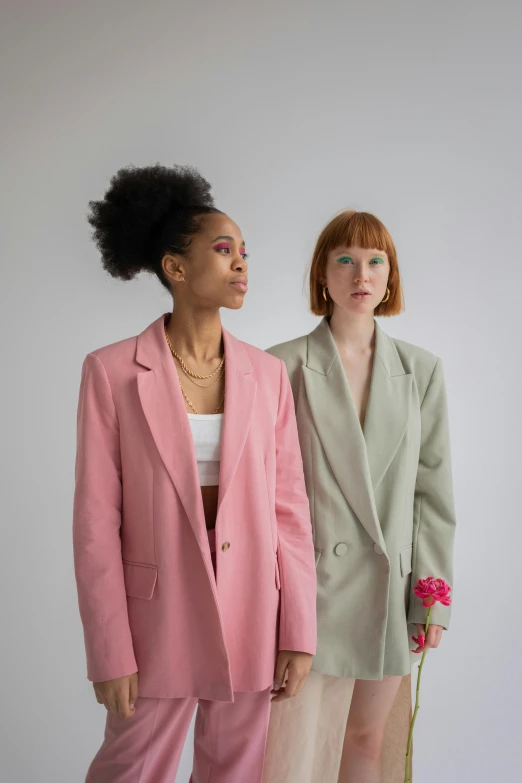 a couple of women standing next to each other, an album cover, by Cosmo Alexander, wearing a light - pink suit, hr ginger, mix of ethnicities and genders, wearing a blazer