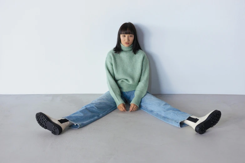 a woman sitting on the floor with her legs crossed, inspired by Kim Tschang Yeul, trending on pexels, wearing a green sweater, japanese collection product, seafoam green, jeans and black boots