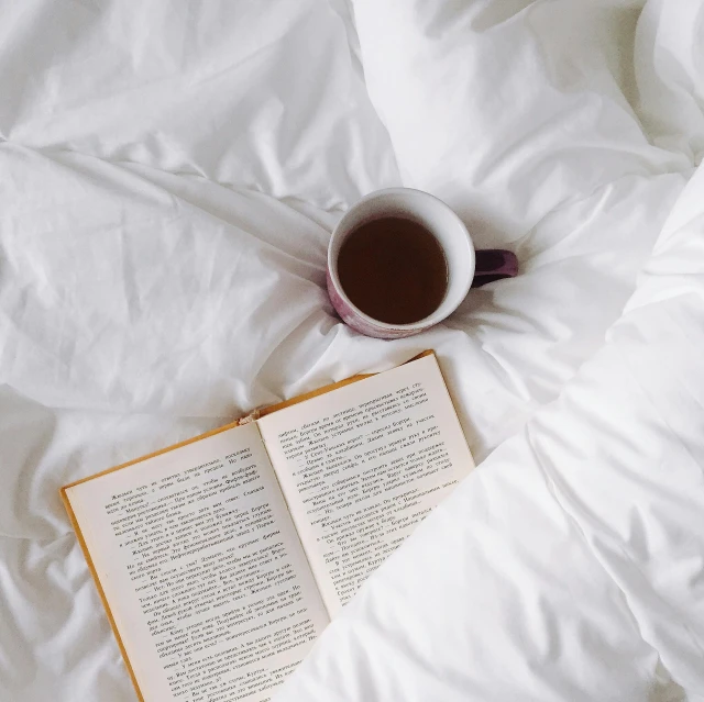 an open book sitting on top of a bed next to a cup of coffee, by Carey Morris, pexels contest winner, romanticism, white bed, bedhead, tea, guide