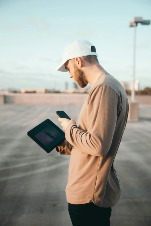 a man standing in a parking lot holding a tablet computer, pexels contest winner, laptops, sunfaded, on a rooftop, phone in hand