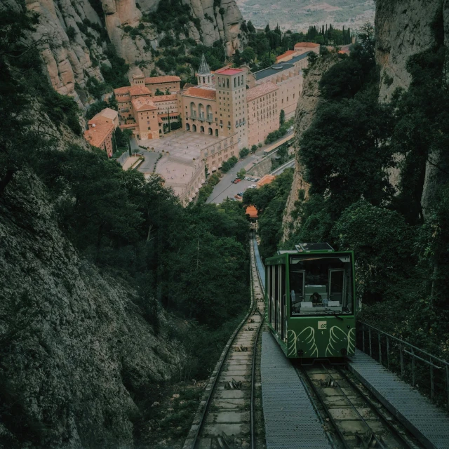 a green train traveling down train tracks next to a mountain, pexels contest winner, art nouveau, monserrat gudiol, elevator, view from the streets, square