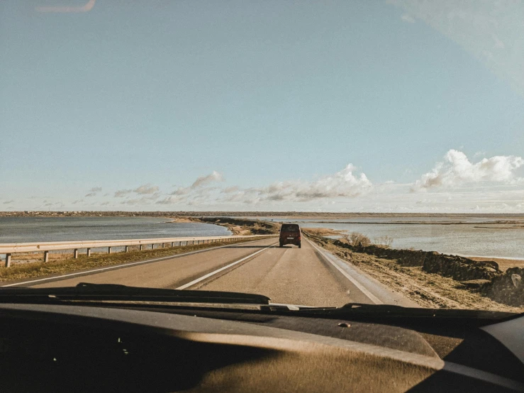 a car driving down a highway next to a body of water, a picture, by Christen Dalsgaard, unsplash, happening, clear skies in the distance, inside a grand, 15081959 21121991 01012000 4k, thumbnail