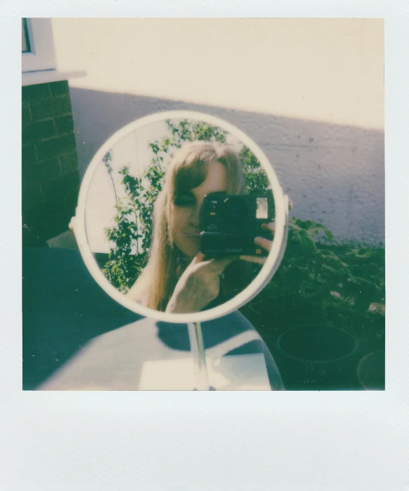 a woman taking a picture of herself in a mirror, a polaroid photo, inspired by Elsa Bleda, happening, pale round face, on a sunny day, soft outlines, a blond