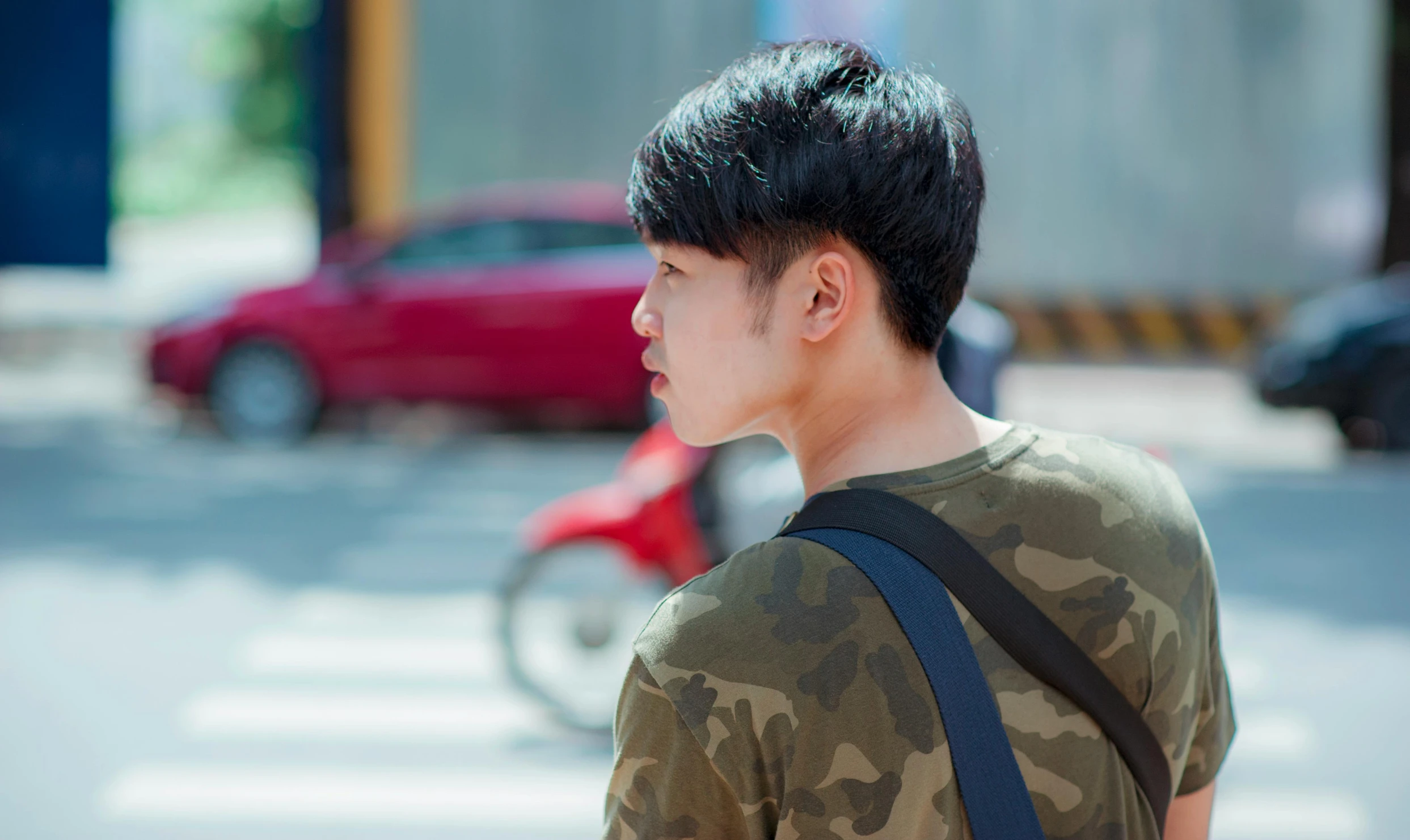 a man with a backpack on a city street, an album cover, inspired by Zhang Han, trending on pexels, camouflage, boyish face, profile view, summer day