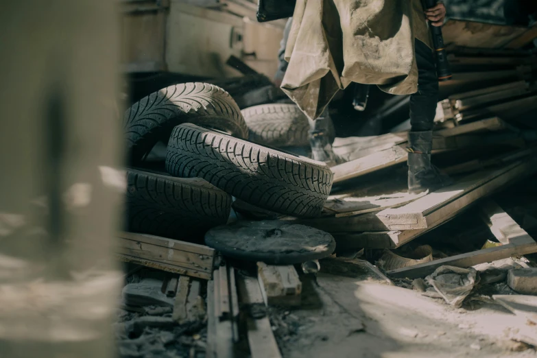 a man standing next to a pile of tires, trending on unsplash, photorealism, collapsed floors, ismail inceoglu and ruan jia, inside a gang hideout, worksafe. cinematic