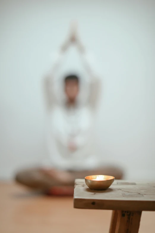 a candle sitting on top of a wooden table, a statue, by Jessie Algie, light and space, padmasana, person in foreground, wooden bowl, light haze