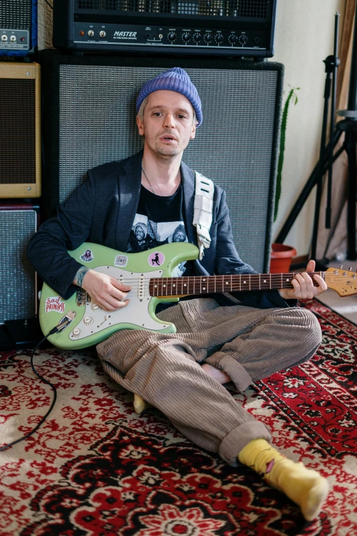 a man sitting on the floor playing a guitar, inspired by Seb McKinnon, smug look, in a studio, promotional image, jesse pinkman