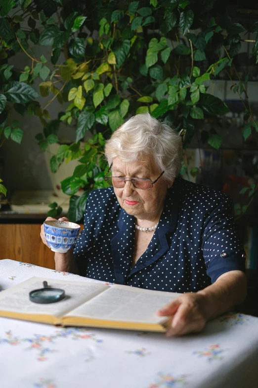 a woman sitting at a table reading a book, by Grytė Pintukaitė, photorealism, botanical herbarium, elderly, next to a cup, museum quality photo