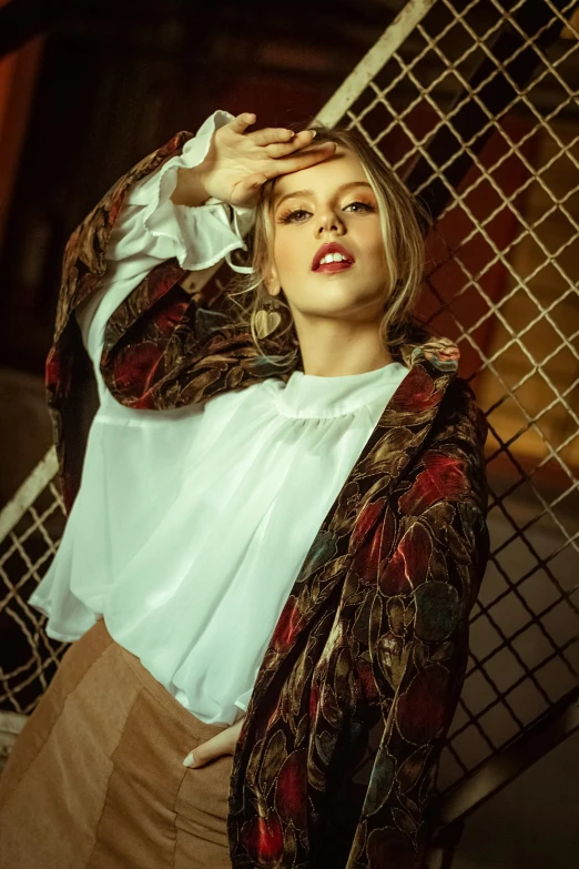 a woman leaning against a fence with her hand on her head, an album cover, inspired by Elsa Bleda, trending on pexels, renaissance, intricate silk clothing, white t-shirt with red sleeves, action glamour pose, a blond
