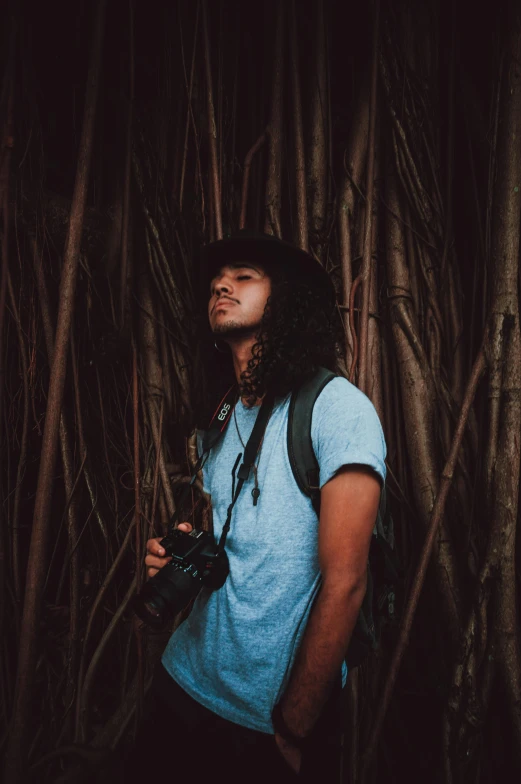 a man standing in a bamboo forest holding a camera, inspired by Jorge Jacinto, a black man with long curly hair, standing with a black background, millennial vibes, profile pic