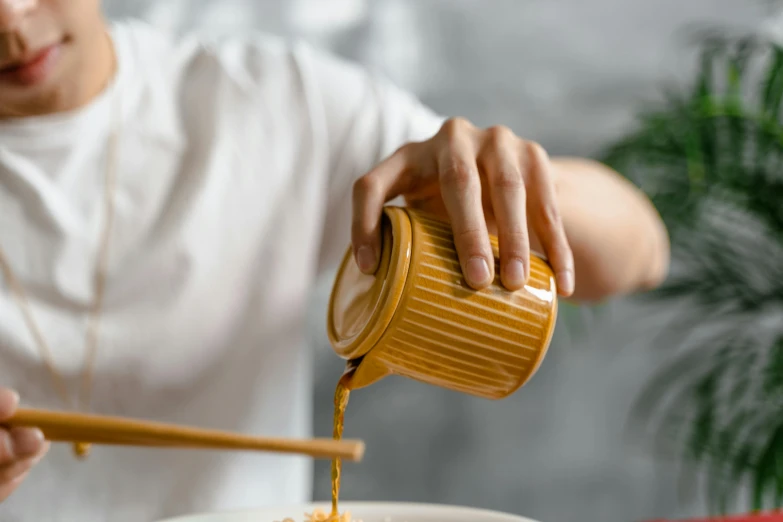 a person pouring food into a bowl with chopsticks, inspired by Kanō Shōsenin, trending on pexels, process art, jar of honey, yellow ochre, porcelain organic, over the shoulder