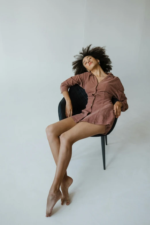 a woman sitting on top of a black chair, wavy hair spread out, sleepy, with brown skin, muted colors. ue 5