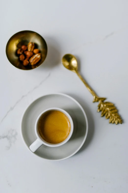 a cup of coffee sitting on top of a white table, inspired by Ceferí Olivé, arabesque, spoon placed, golden raito, next to a cup, premium