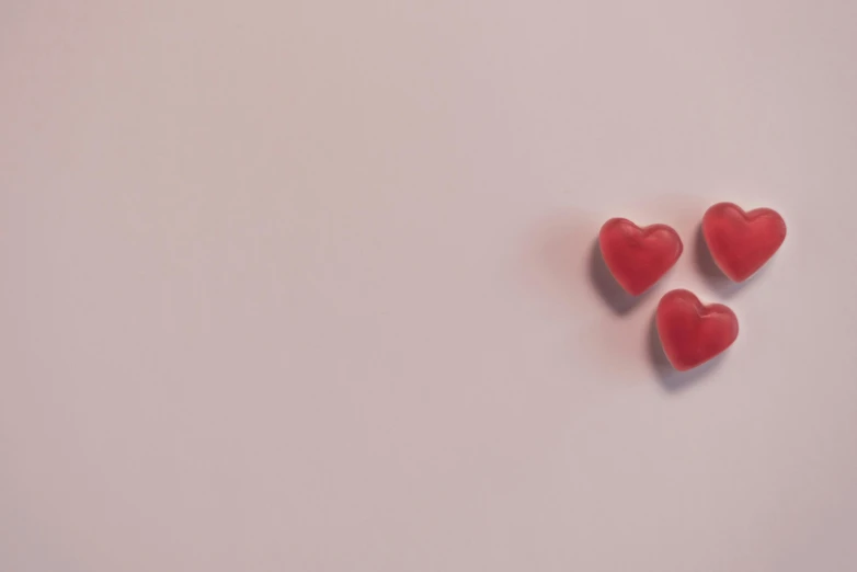 a couple of red hearts sitting on top of a white surface, a picture, by Emma Andijewska, pexels, pink background, made of candy, threes, gif