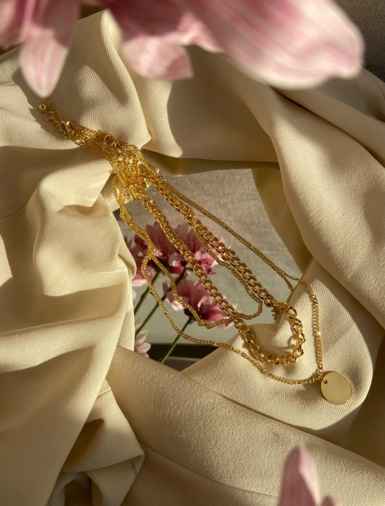 a bunch of pink flowers sitting on top of a white cloth, multiple golden necklaces, 1990s photograph, 10k, shot on iphone 1 3 pro max