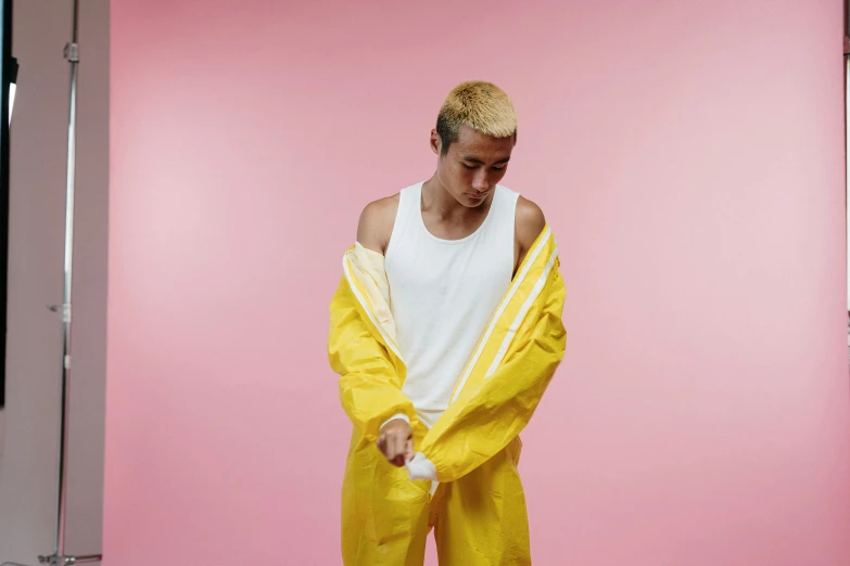 a man standing in front of a pink background, an album cover, inspired by Russell Dongjun Lu, trending on pexels, hyperrealism, yellow raincoat, wearing dirty overalls, genderless, wet floor