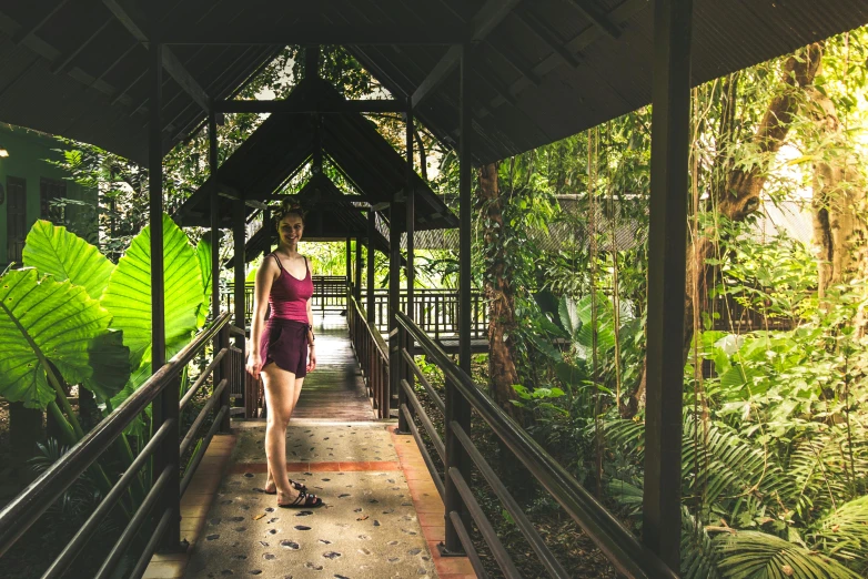 a woman in a pink dress walking down a walkway, unsplash, tribe huts in the jungle, paradise garden massage, malaysia jungle, avatar image