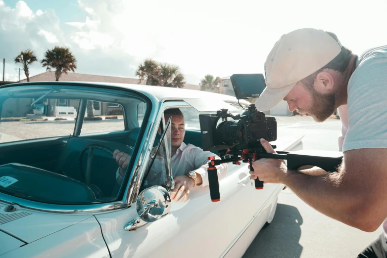 a man that is sitting in a car with a camera, meet the actor behind the scenes, unsplash photography, vhs footage of a movie set, cinematic mid shot fight