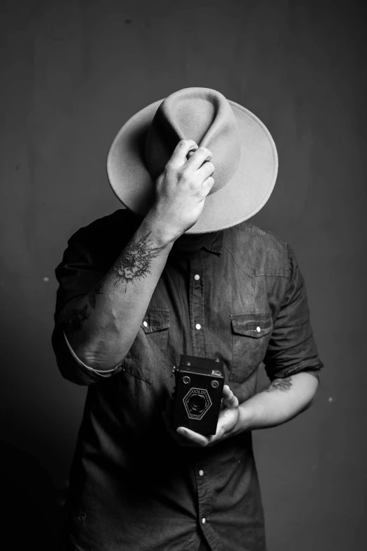 a man wearing a hat and holding a camera, a black and white photo, by Tom Bonson, dustin panzino, jony ives, eric lacombe, cowboy