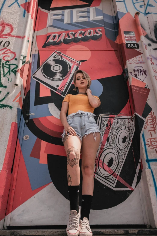 a woman standing in front of a wall covered in graffiti, an album cover, trending on pexels, graffiti, round thighs, dj set, gen z, charts