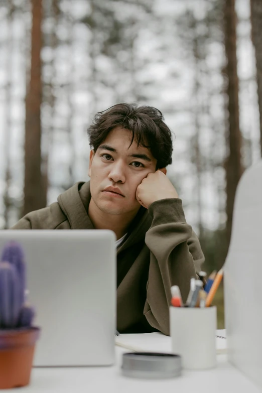 a man sitting in front of a laptop computer, by Jang Seung-eop, trending on pexels, realism, pouty face, trees in the background, studious, stern expression