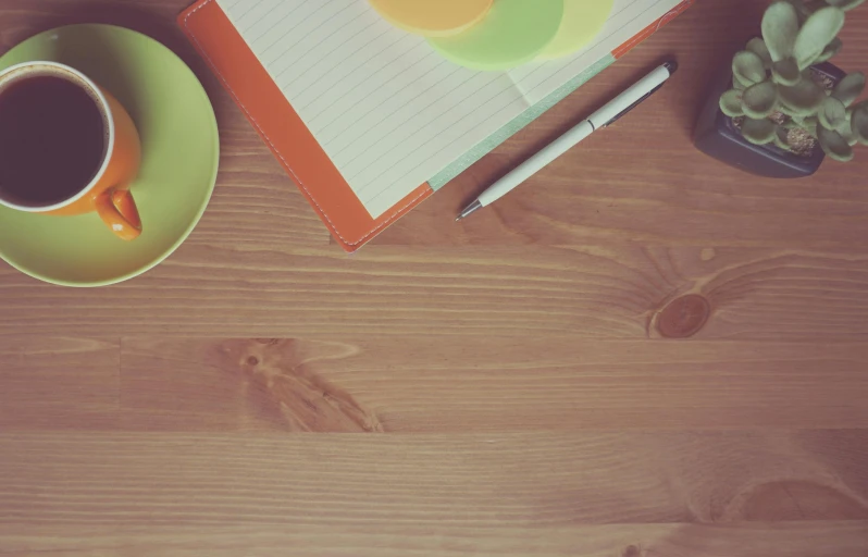 a notepad sitting on top of a wooden table next to a cup of coffee, pexels, chartreuse and orange and cyan, 9 9 designs, background image, kitchen table