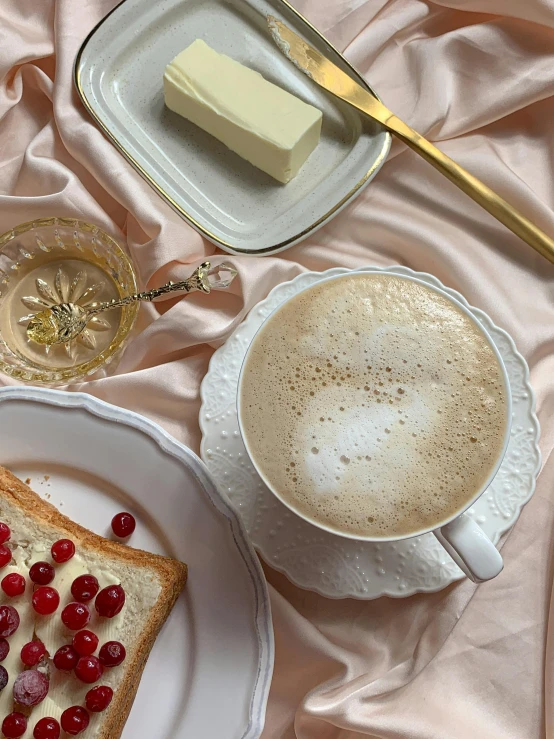 a white plate topped with a piece of bread next to a cup of coffee, trending on instagram, romanticism, gold and pearls, thumbnail, soymilk, white and pink cloth