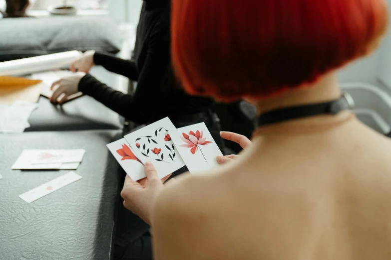 a woman sitting at a table holding playing cards, a tattoo, by Julia Pishtar, pexels contest winner, hanafuda, pair of keycards on table, on a white table, one is a redhead